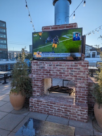 Outdoor television mounted above a brick fireplace on a commercial rooftop patio